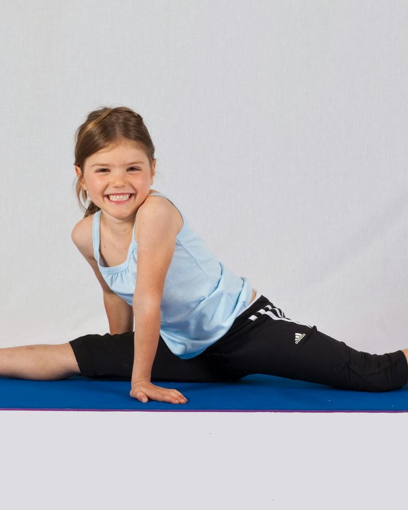 Smiling child in a simple yoga pose on a colorful mat.